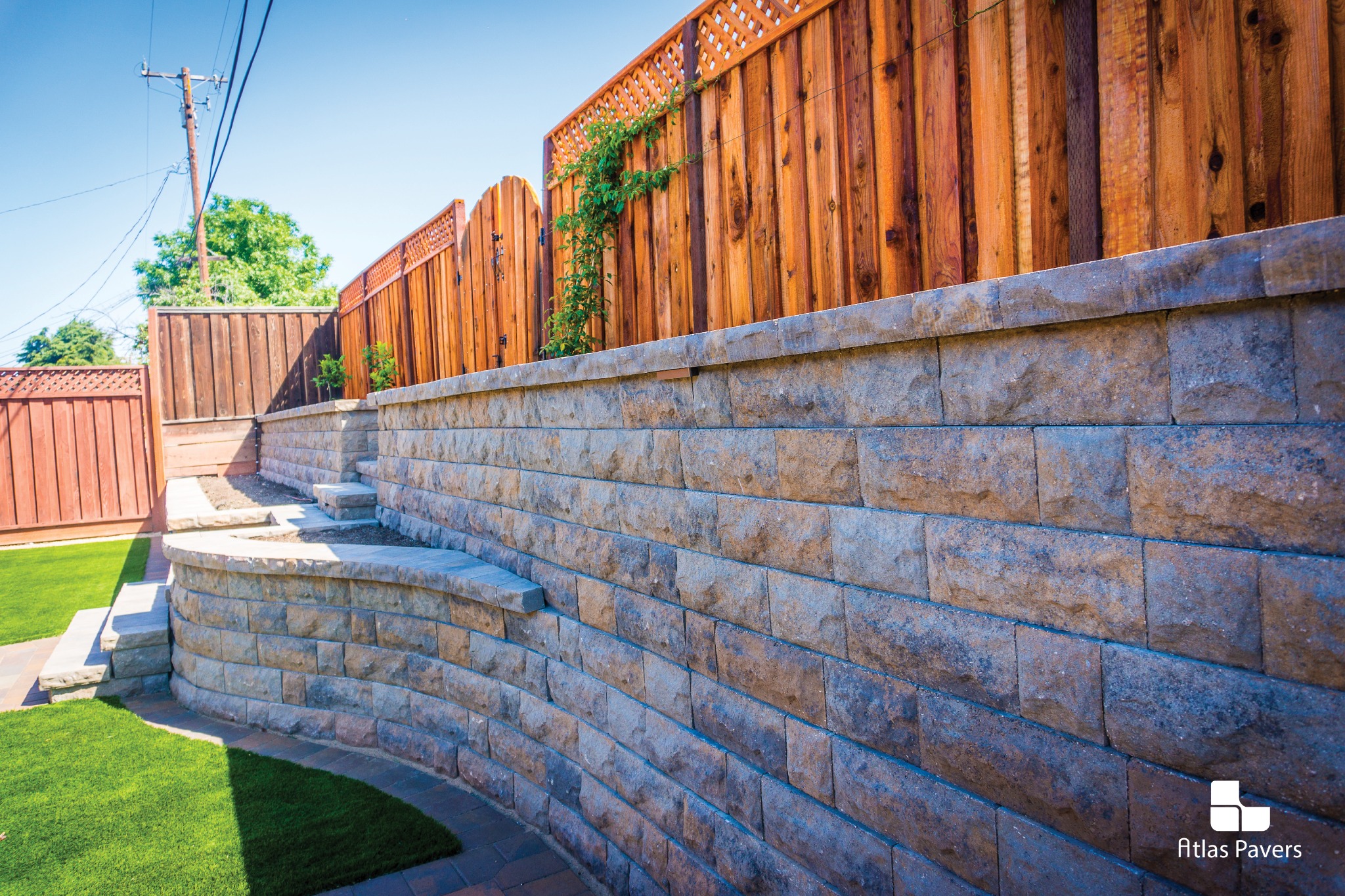 Atlas Pavers block retaining wall beside a lawn and wood fence